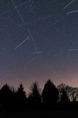 Fransa 'nın Dordogne bölgesindeki bir orman üzerinde gece gökyüzünde kayan yıldızların ve uyduların birleşimi