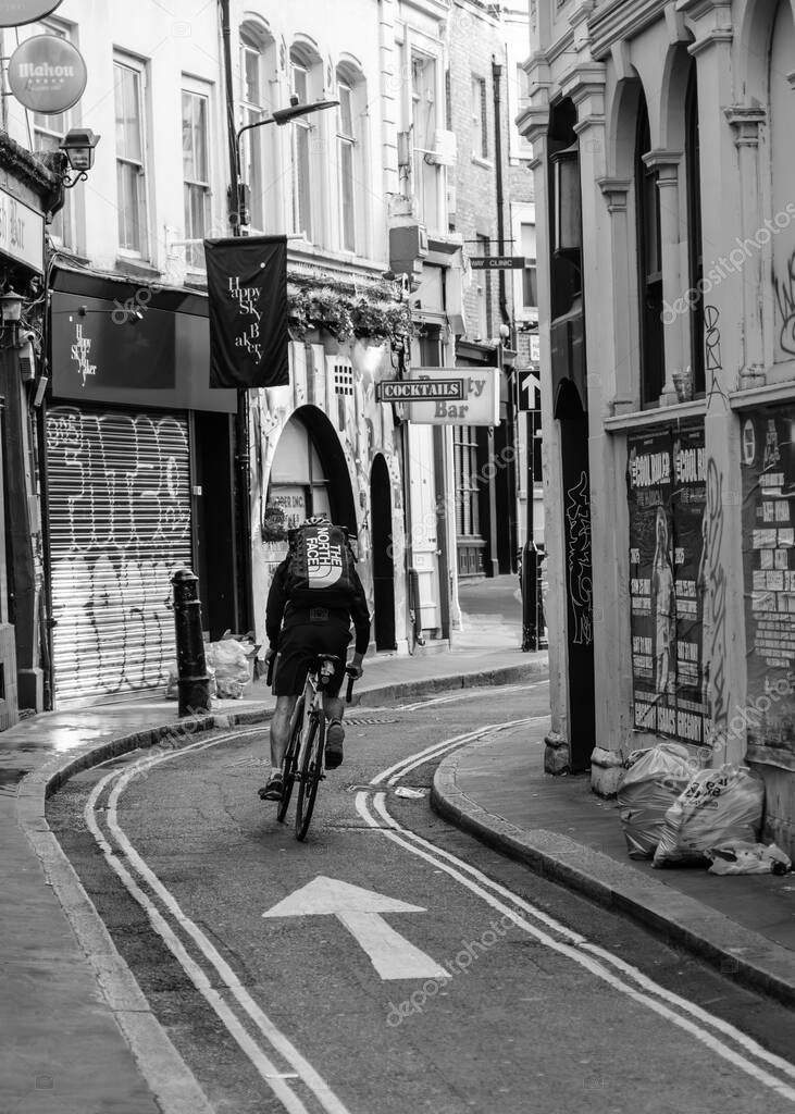 London, England - 28th April 2025: A cyclist with a backpack rushes along Hanway Street in Central London