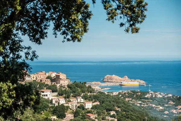 Ile Rousse, Corsica, Fransa - 25 Mayıs 2025: Bir Korsika feribotu Akdeniz 'in Korsika adasındaki Ile Rousse limanında ön planda Monticello köyü ile birlikte yer almaktadır.