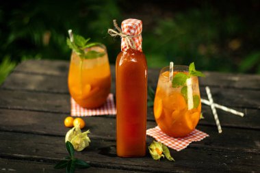 Kayısı cam bir şişe içinde ev yapımı limonata ve doğada ahşap masa üzerinde meyve ve süsleme ile