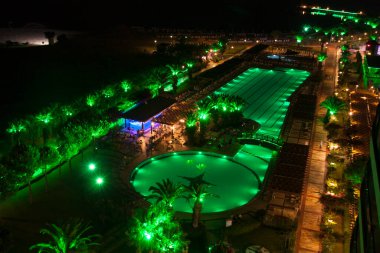 Deniz kenarındaki şehir palmiyeleri ve gece aydınlatma fotoğrafında yüzme havuzu.
