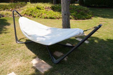 Sahildeki hamak boş beyaz hamak, tropikal plaj fotoğrafında çam ağaçları arasındaki gölgede güneş şapkası.