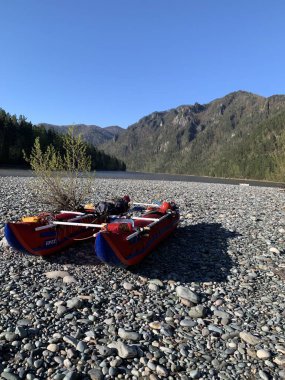 Katun Nehri kıyısındaki kırmızı tekne Altai Cumhuriyeti, Rusya. Etrafı yeşil ağaçlarla, mavi dağlarla çevrili. Mavi gökyüzü, beyaz bulutlar, parlayan güneş. Boş tekne maceraya hazır..