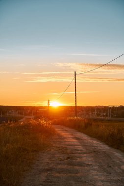 Rural country road at the beautiful summer sunset nature landscape. Empty road and tranquil evening scene with warm sunlight. The dramatic sky above the farm.