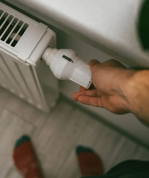Close-up of turning down the thermostat on a radiator to save energy due to heating cost price hike. Concept of economizing cost during cold weather and energy crisis.