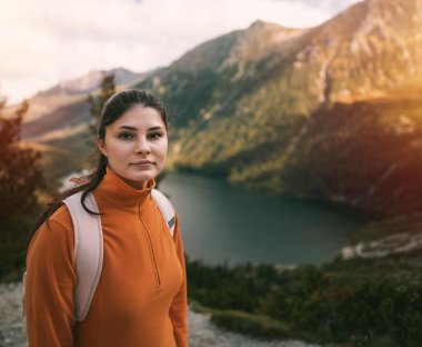 Dağın tepesinde sportif bir kadın. Dağlarda gündelik yürüyüş. Güzel gökyüzü, göller, ormanlar ve dağ zirveleri