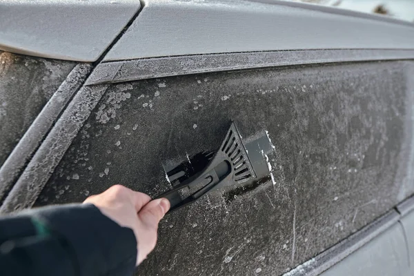 Scraping off the ice from the frozen car window. Winter season car. Ice scraper POV