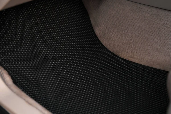 Luxury car with white leather interior with high-quality EVA floor mats in black color. Close-up of black ethylene vinyl acetate car floor mat.