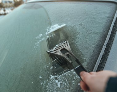 Cleaning the windshield from ice with a plastic ice scraper.