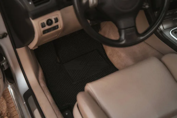 Driver-side black floor mats made of ethylene vinyl acetate shortened for EVA. Dark floor mats in the light interior of the car.