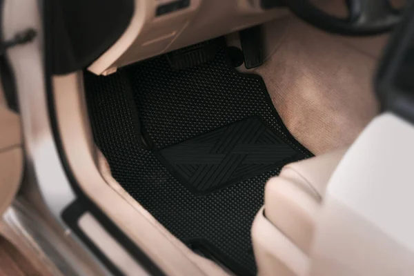 Luxury car with white leather interior with high-quality EVA floor mats in black color. Close-up of black ethylene vinyl acetate car floor mat.