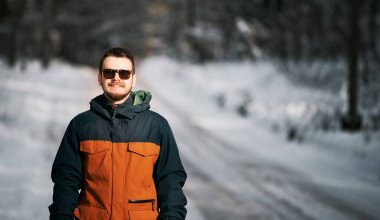 Bearded man in the winter forest. Guy wearing sunglasses during snowy weather.