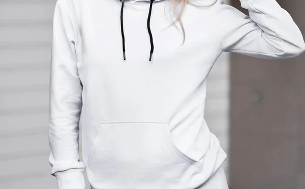 Design mock-up for clothing logo. A woman wears a white hoodie on the street.
