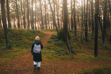 Woman with a backpack walking in the park. Concept of traveling alone and outdoors discovering. Person in the forest.