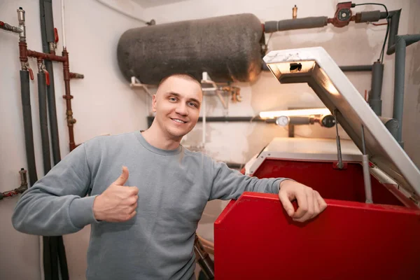 Industrial system engineer shows off his smile while fixing the heating system. Caucasian engineer recommends to use sustainable heating systems