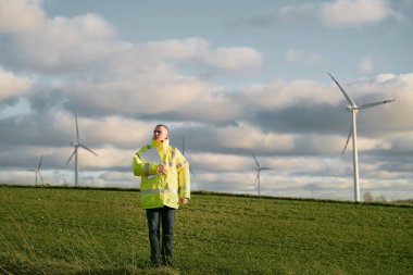 Erkek bir mühendis, rüzgar türbini tarlasında duruyor. Çok güzel bir arka planı var. Sürdürülebilir gelecek kavramı.