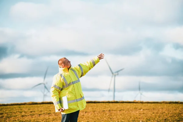 Man pointing at the sky while standing near wind turbines. Sustainable future and renewable power sources concept.