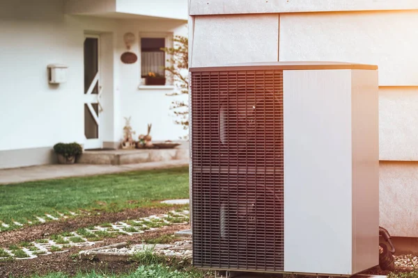An air conditioner outdoor unit outside of a house in the grass. Modern HVAC and heat pump system
