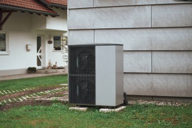 Bahçesinde sıcak su pompası olan beyaz bir ev. Maliyet etkin ısıtma sistemi kavramı