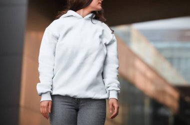 Genç bir kız beyaz bir kapüşonlu giyiyor. Temel spor giyim logosu yok. Uzun kollu kazak modeli..