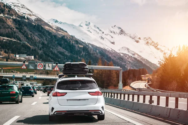 White wagon with roof box storage on the highway in Switzerland. Modern family car adventures in the Alpine Mountains in Europe. Plastic luggage compartment on a car roof. Road trip getaway concept.