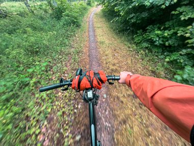 Şehirdeki orman yolunda güneş ışığına doğru bisikleti kullanmanın birinci şahıs görüntüsü. Bisikleti spor ve eğlence amaçlı kullanma kavramı..