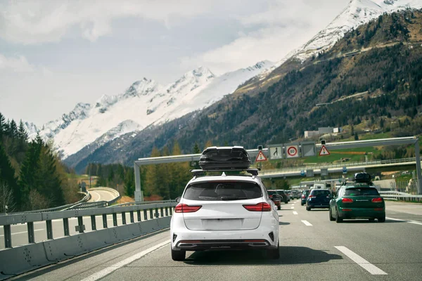 Rear view of a car with a roof box. Black luggage compartment box on a sport white car, back view. Alpine highway. Black Roof Box on a Sporty White Wagon Family Car