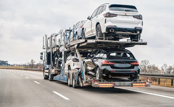 Car transporter carries new luxury vehicles along the motorway, back view of the trailer. Big car carrier truck of new sport german cars delivery to dealership. truck of new powerful new vehicles.
