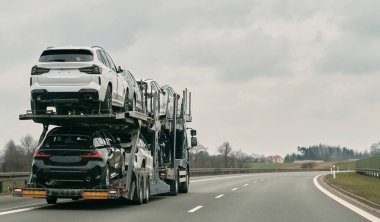 Taşıyıcı, otobanda yeni lüks araçlar taşıyor. Karavanın arka görüntüsü. Yeni Alman spor arabalarından oluşan büyük bir kamyon bayiliğe teslim edilecek. Yeni güçlü araçlar kamyonu.