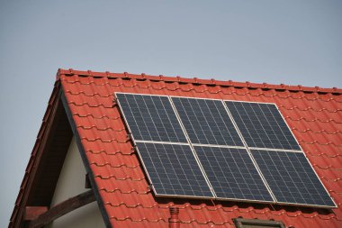 Üzerinde güneş paneli olan kırmızı bir çatı. Çevre koruma ve sürdürülebilir enerji kaynakları kavramı.