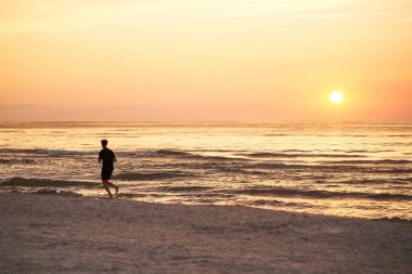 Okyanus Günbatımında koşan bir sporcunun silueti. Güneşe karşı koşan bir kişi.