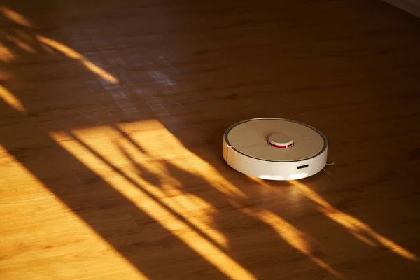 Vacuum cleaner cleans the floor. Robotic vacuum cleaner is on a laminate wooden floor. Smart home, housework, cleaning technology concept. Copy space. Smart Home Cleaning.