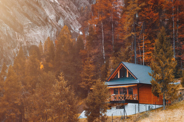Wooden house in beautiful nature. Mountain style house. Pretty landscape with modern wooden house surrounded by trees with colorful foliage and mountains. Runaway chalet cabin in the forest.