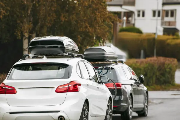 Rooftop cargo carrier bag. Rear view of a car with a roof box. Parked cars in Europe. Black Roof Box on a Sporty White Wagon Family Car. Removable black car trunk for luggage on the roof of a car.