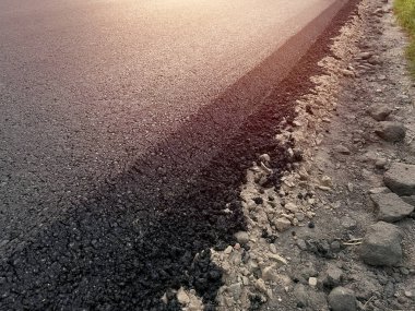 Yeni yoldaki taze sıcak asfaltın yakın çekim dokusu. Yol yapımı. Büyük bir katman taze asfalt. Sığ bir alan derinliğinde asfalt ham madde katmanı.