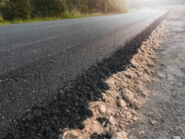 Yeni yoldaki taze sıcak asfaltın yakın çekim dokusu. Yol yapımı. Büyük bir katman taze asfalt. Sığ bir alan derinliğinde asfalt ham madde katmanı.