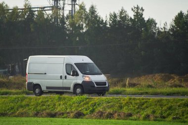 Yolda beyaz bir minibüs var. Kargo ve paketleri depodan müşterilere taşıyor. Lojistik servislerinin tasarımlarını ve markalarını gösteriyor..