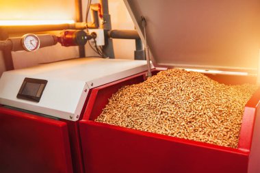 Sıkışmış ahşap topakları yeşil ve ekonomik yakıt kaynağı olarak kullanan bir pelet sobası, ateş ve teknolojiyle yerli bir fırını ısıtıyor..