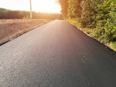 Yeni inşa edilmiş bir yoldaki sıcak ve taze asfalt tabakasının yakın görüntüsü, malzemenin dokusunu ve tahılını ve kaldırım yapımında kullanılan ekipmanı gösteriyor. Kaldırım inşaatı ve döşenmesi