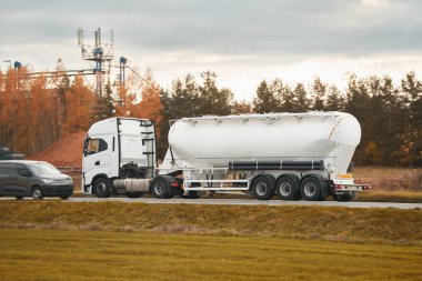 Propan tanklı yarı kamyon asfalt yolda ilerliyor. ADR tehlikeli kargo, yan görüş. Tehlikeli malları taşıyorum. Tehlikeli madde tankında yüksek sıcaklıkta sıvı tehlike ve çeşitli tehlike etiketleri var.