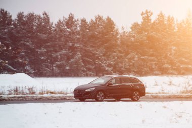 Arabayla kış gezisi. Kar ve buzla kaplı kış yolundaki araba. Araba kış lastikleriyle donatılmıştır ve biraz kar ve su sıçratmaktadır. Otobanda karlı bir manzara.