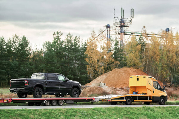 A tow truck evacuates a broken pick-up truck on a flatbed trailer from the interstate highway, after an accident that required emergency service and assistance.