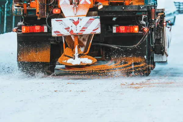 A snowplow truck applies salt and sand as the truck works to clean the snowy road. Roads and infrastructure maintenance during winter time. Rust and damage to vehicle undercarriage.