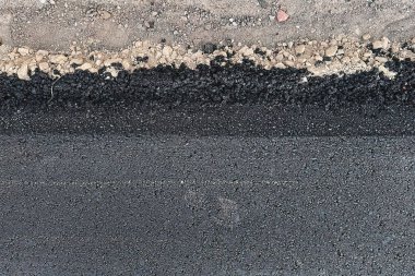 Yeni inşa edilmiş bir yoldaki sıcak ve taze asfalt tabakasının yakın görüntüsü, malzemenin dokusunu ve tahılını ve kaldırım yapımında kullanılan ekipmanı gösteriyor. Kaldırım inşaatı ve döşenmesi