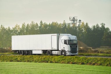 Bir yük kamyonu bir konteynırı otoyolda taşır. Avrupa konseptinde lojistik. Arkasında güzel kırmızı bir güneş batarken bir otoyolda kargo kamyonu sürüyorum..