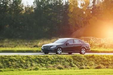 Günbatımı ve orman geçmişi olan lüks spor bir arabada hız yapmak. Entellektüel pahalı araba yolda. Otobanda lüks ve lüks bir araba var..