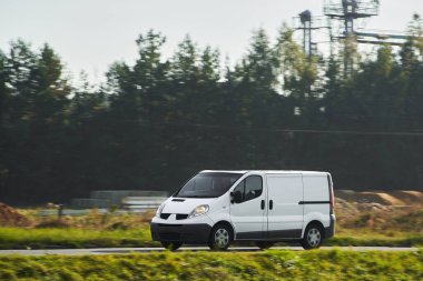 Yolda beyaz bir minibüs var. Kargo ve paketleri depodan müşterilere taşıyor. Lojistik servislerinin tasarımlarını ve markalarını gösteriyor..