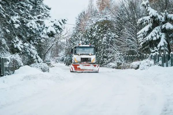 A snowplow truck clears the highway from snow during a winter storm. Snow blowing out of the plow as a truck works to clean the icy road. Roads and infrastructure maintenance during winter time.