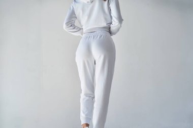 Beyaz, minimalist eşofman altı giyen genç bir kadının arkası. Şık, beyaz bir kıyafetle konfora girin. Sıradan zarafet için mükemmel. Spor giysi modeli. Beyaz pantolonlu kız..