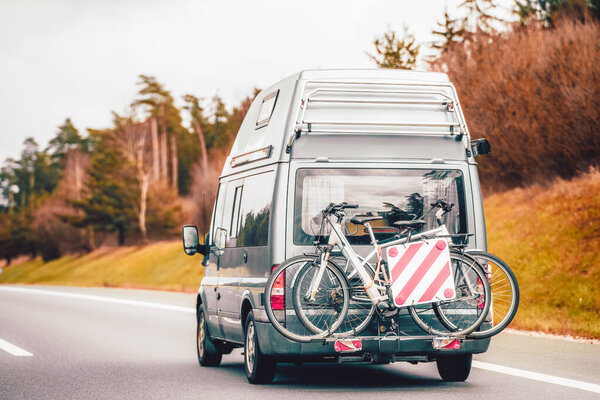 Семейный отдых в Европе. Современный белый фургон с велосипедной стойкой на заднем плане путешествует по шоссе с живописным ландшафтом.